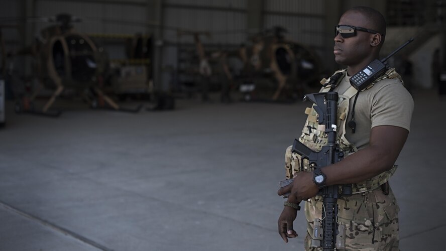 Senior Airman Micheal Thomas, 738th Air Expeditionary Advisory Group guardian angel, provides armed overwatch for contractors and air advisors performing maintenance on an Afghan Air Force MD-530 Light Attack Helicopter, April 16, 2017, at Kandahar Air Wing, Afghanistan. Thomas is deployed with other Citizen Airmen from the 507th Security Forces Squadron, Tinker Air Force Base, Okla. (U.S. Air Force photo/Staff Sgt. Katherine Spessa)