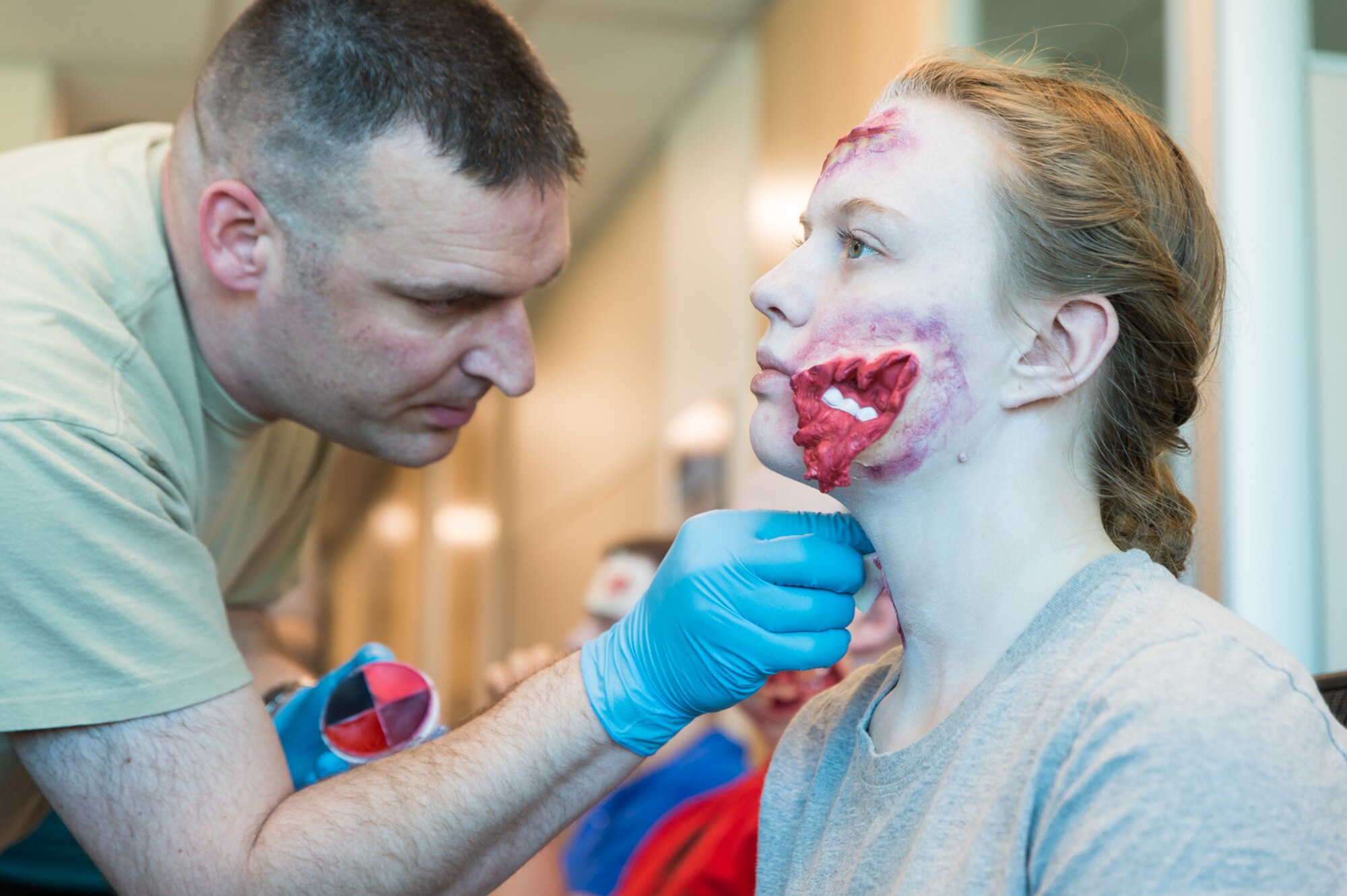 U.S. Air Force Chief Master Sgt. Jeremy Nash with the 153rd Medical Group applies moulage to Airman 1st Class Heather Peters to train medics to create realistic wounds. Nash used this opportunity to also create zombies for recruiting material which will be used at Cheyenne's upcoming Comic Con in May. (U.S. Air National Guard photo by Senior Master Sgt. Charles Delano/released)
