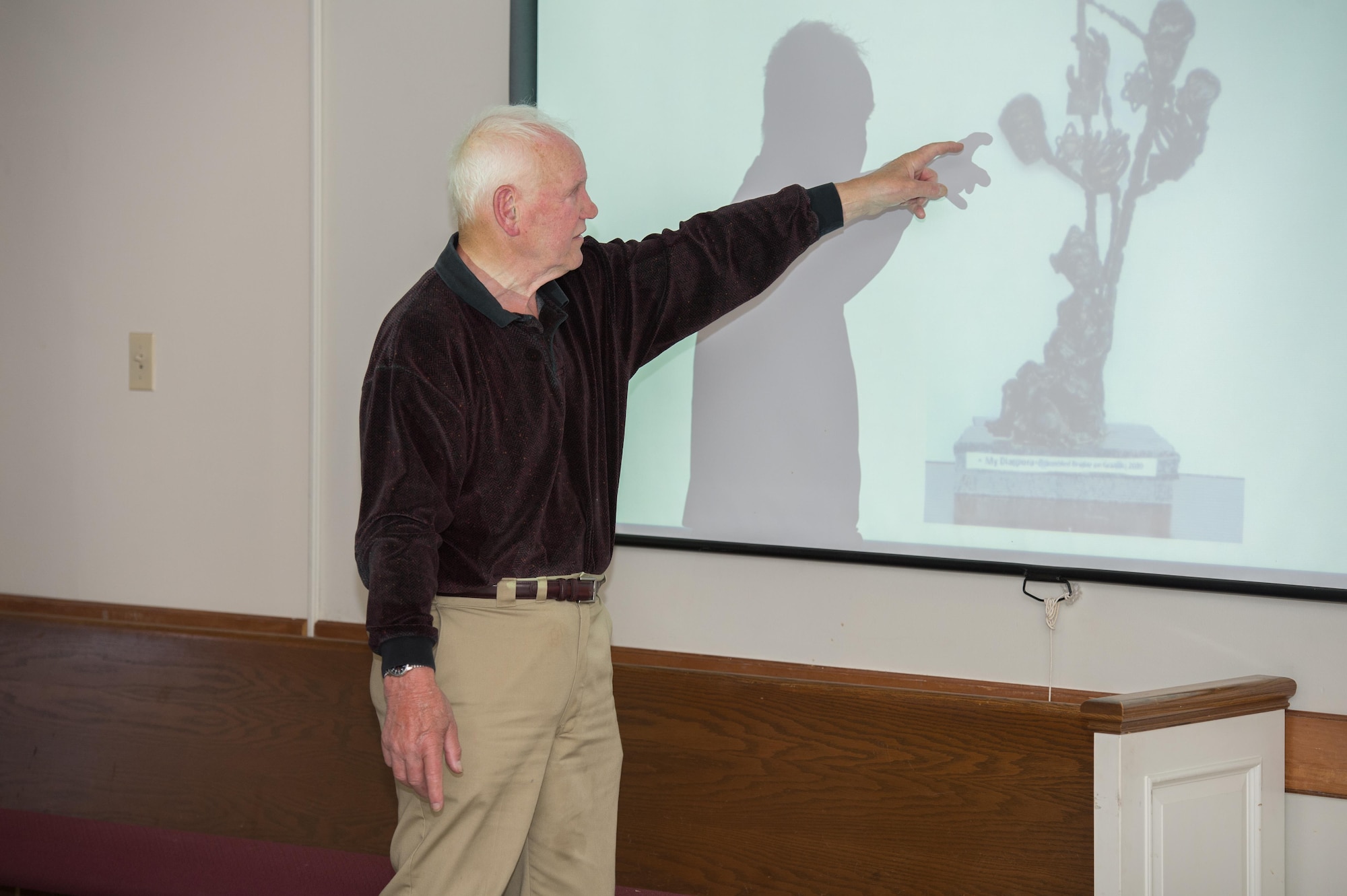 Fred Manasse, a Holocaust survivor, shows a photo of a sculpture he did to memorialize his family to approximately 50 attendees of his speech during Holocaust Remembrance Week at Hanscom Air Force Base, Massachusetts, April 24. Manasse is a retired systems engineer who is now active with national Holocaust survivors organizations, having survived seven years fleeing Nazi persecution in Europe from 1938-1945. (U.S. Air Force photo by Jerry Saslav)