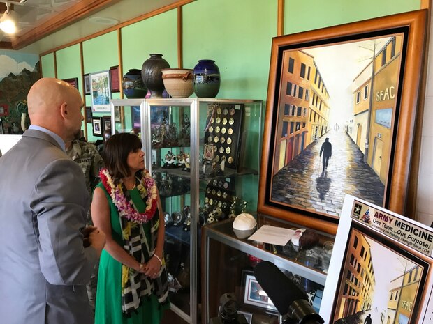 The Second Lady of the United States, Karen Pence, views a painting created by a spouse of a 25th ID Soldier, Cindy Manga, April 24, 2017.  The painting depicts a shadowed figure, a Soldier with a cane walking down a dark hallway. As the hallway goes on, it gets lighter. At the end of the tunnel is the source of the light: the Soldier's wife and two children awaiting him and supporting him through his journey. On the left side wall in the scene are rooms with each department that helped the family through. On the right, a sign that reads: SFAC, which stands for Soldier and Family Assistance Center. Pence also visited with military and civilian leaders during a tour hosted by U.S. Health Clinic at Schofield Barracks, to talk about how art therapy is being used to help military members and their families deal with difficulties, disabilities or diagnoses. The tour took place outside of the clinic's walls to where art therapists and patients have unfettered access to their tools: Pens, paper, brushes, ceramics and more. Pence, who is a champion for art therapy programs, visited the arts and crafts building on Schofield, where she spoke with patients currently enrolled in art therapy programs.