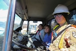 Pfc. Amanda Schmidling, a horizontal construction engineer with the Arizona National Guard’s 259th Engineer Platoon, drives local school students around during their visit to the Innovative Readiness Training runway extension project at Old Harbor, Alaska, April 20, 2017. 