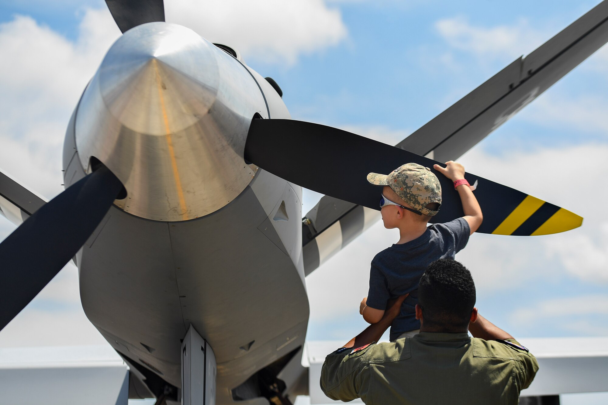 An Airman assigned to the 432nd Wing/432nd Air Expeditionary Wing lifts a child in the air to feel the propeller of the MQ-9 Reaper model during the 2017 Gulf Coast Salute Open House and Air Show April 22, 2017, at Tyndall Air Force Base, Fla. The MQ-9 model stood among other aircraft displays for the first time and provided air show visitors a visual of the MQ-9. (U.S. Air Force photo/Airman 1st Class James Thompson)