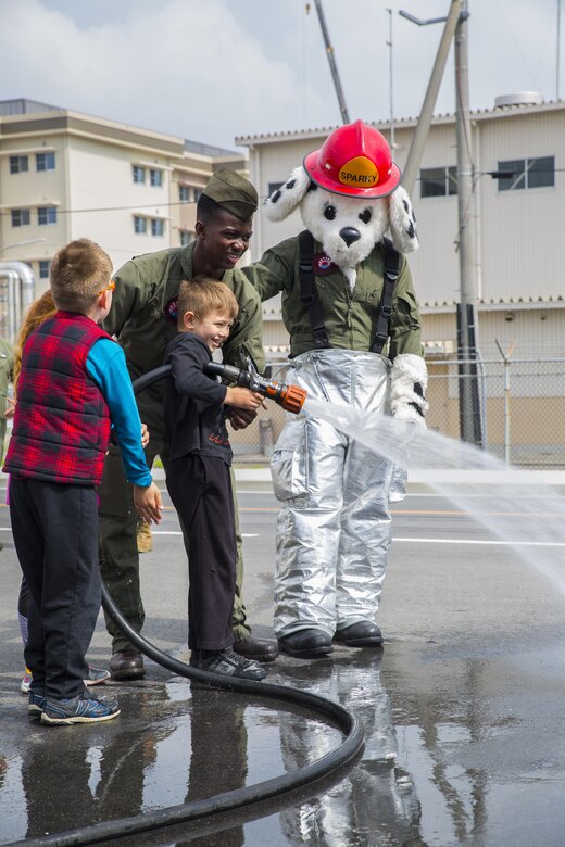 U.S. Marine Corps Lance Cpl. Akeem Mcfarlane, aircraft rescue firefighter with Headquarters & Headquarters Squadron teaches Gabriel Keller, a Junior Recruit Day participant, how to use a fire hose during the Aircraft Rescue and Firefighter training portion of Marine Aircraft Group 12’s Junior Recruit Day at Marine Corps Air Station Iwakuni, Japan, April 21, 2017. The purpose of Junior Recruit Day is to increase family readiness in the community by showing children and young adults what their parents do on a daily basis. (U.S. Marine Corps photo by Mason Roy)