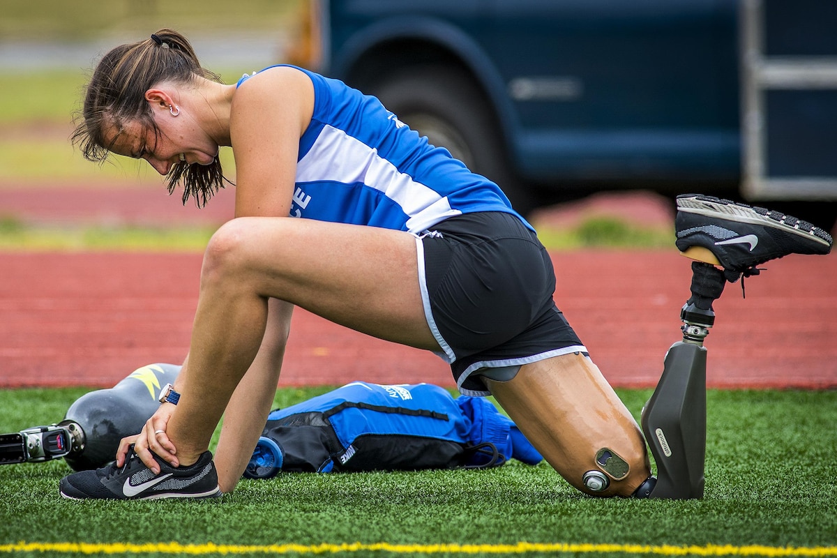 A female athlete with a prosthetic leg stretches after a run.