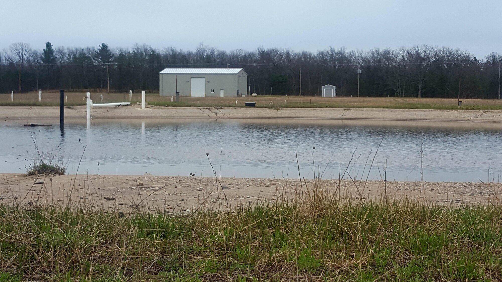 Former Fire Training Area #2 was operated at Wurtsmith Air Force Base, Michigan, from 1958-1991. The training area where the base conducted weekly fire training exercises is a known release location of AFFF - a firefighting agent used to extinguish fuel fires. Pictured above is the 115-foot diameter circular pit constructed with six-inch thick reinforced concrete and underlain by polyethylene sheeting. Building in the background houses a pump and treat remediation system the Air Force installed in April 2015 to cut off contaminant discharges into nearby Clark’s Marsh. (Photo by Breanne Humphreys/ Air Force Photo Released)