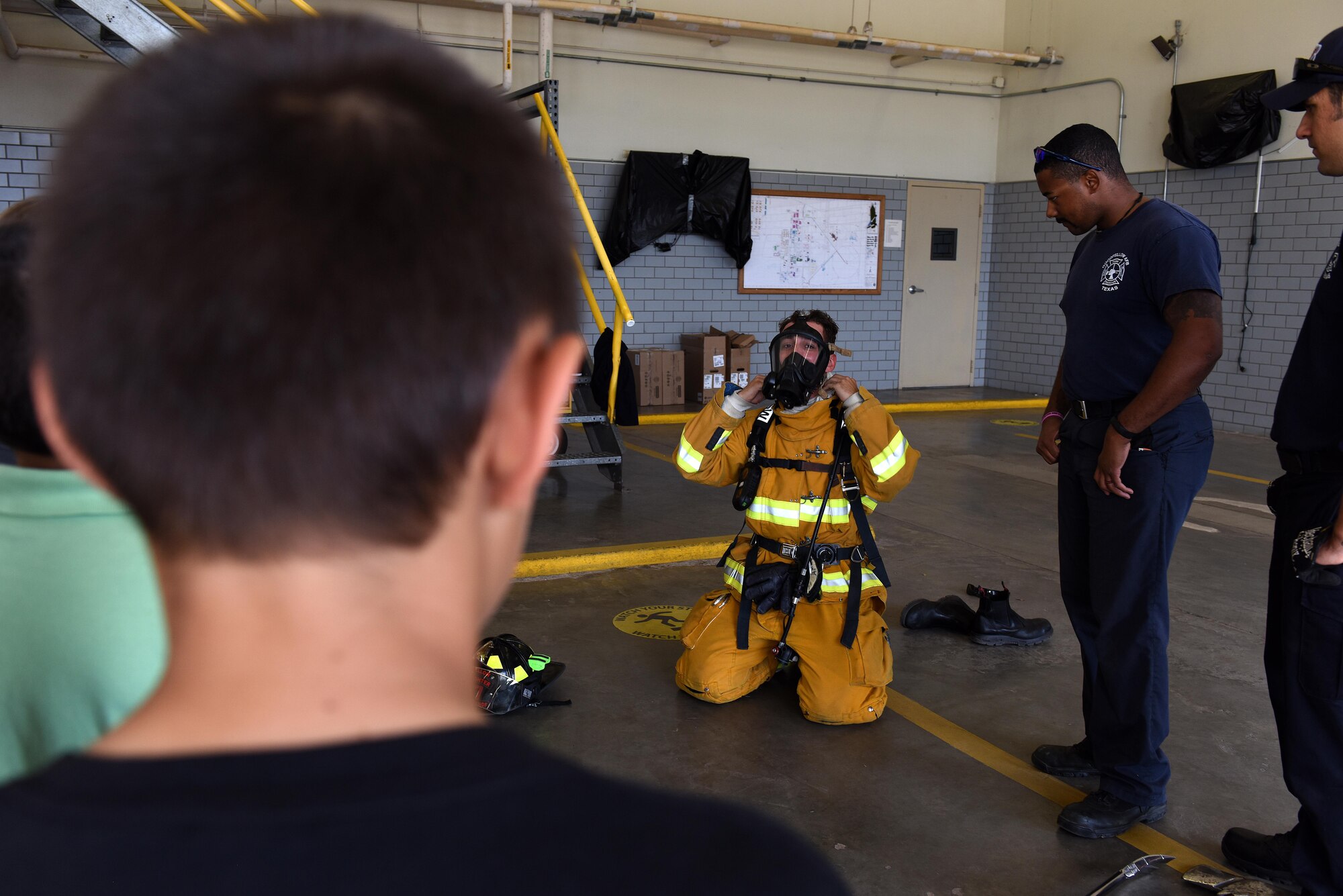 A child watches fire protection professionals demonstrate how to put on bunker gear at the Goodfellow fire department on Goodfellow Air Force Base, Texas, April 28, 2017. The fire protection professionals also taught them about the necessity of motion sensors and air tanks. (U.S. Air Force photo by Airman 1st Class Caelynn Ferguson/ Released)