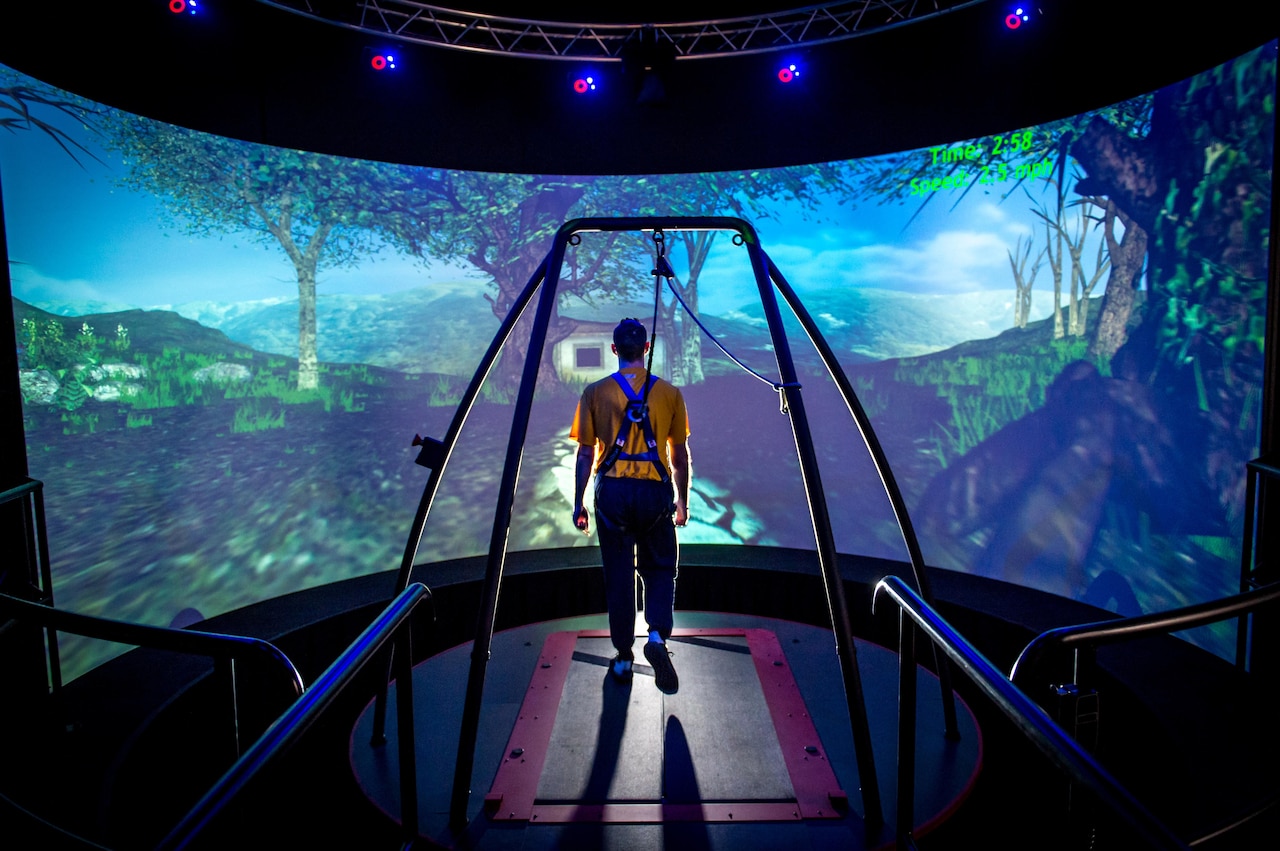 A traumatic brain injury patient walks through a virtual reality scenario at the Computer Assisted Rehabilitation Environment Laboratory at National Intrepid Center of Excellence at Walter Reed National Military Medical Center in Bethesda, Md., March 20, 2017. The patient is attached to a safety harness and walks on a treadmill on a platform that moves and rotates in conjunction with movements of the projected environment. Motion capture cameras track the patient’s movements via reflective markers that are applied to the patient and supply data on physical deficits to physical therapists. Air Force photo by J.M. Eddins Jr.