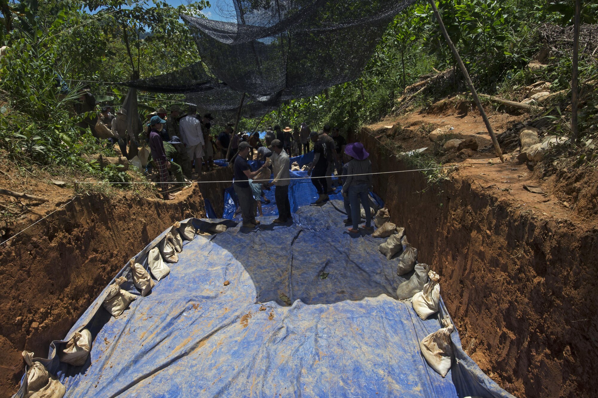 U.S. service members work alongside Vietnamese personnel to place sandbags on the edge of a tarp to keep the soil inside of excavated units dry in Phuoc Son providence, Vietnam, June 6, 2016. The mission of DPAA is to provide the fullest possible accounting for our missing personnel to their families and their nation. (U.S. Air Force photo by Staff Sgt. David Owsianka) 