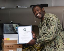 MANAMA, Bahrain (July 27, 2017) Information Systems Technician 2nd Class Lucian Matthias, assigned to U.S. Naval Forces Central Command, poses for a photo after having been administered the oath of enlistment by his brother Army Maj. Leon H. Matthias Jr., assigned to 532nd Military Intelligence Battalion, 501st Military Intelligence Brigade in Camp Humphreys, South Korea, on screen, via a video teleconference. (U.S. Navy photo by Mass Communication Specialist 2nd Class Victoria Kinney)