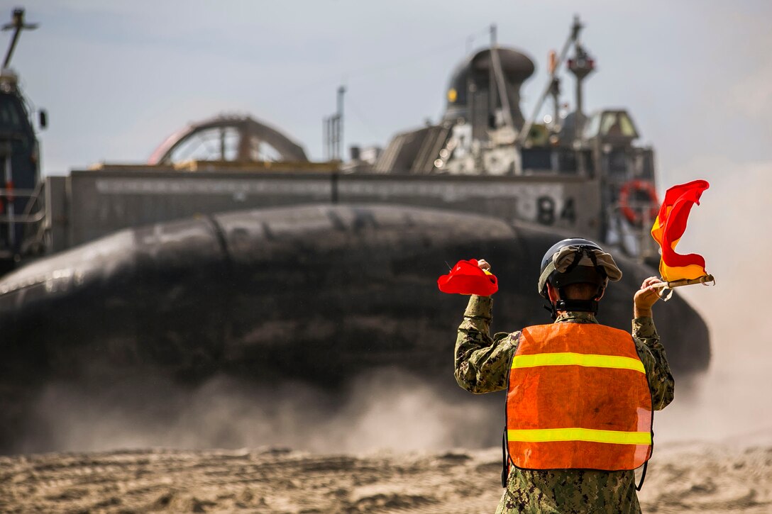 A U.S. Navy beachmaster signals a landing craft, air cushion ashore during Amphibious Squadron (PHIBRON) -Marine Expeditionary Unit (MEU) Integration Training (PMINT) at Onslow Beach, N.C., July 10, 2017. PMINT allows the Navy-Marine Corps team to improve interoperability and exercise the unique capabilities of the Amphibious Task Force. 