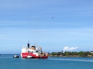USCGC HEALY departs Honolulu, flanked by two tug boats.