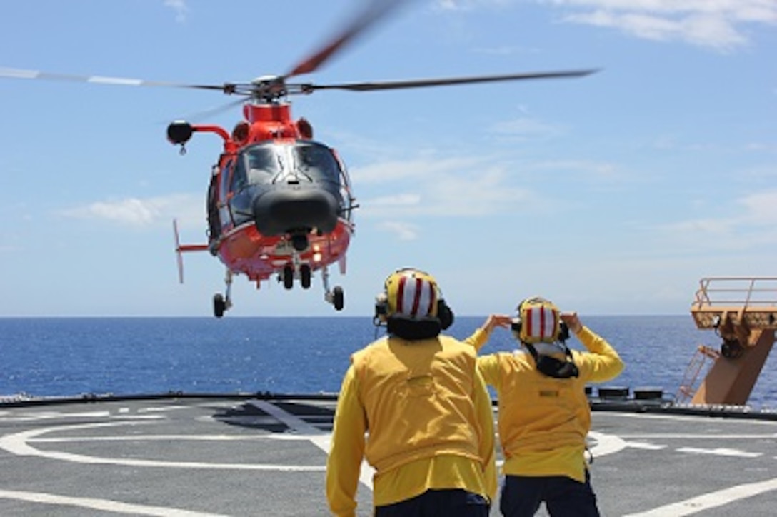 Landing Signal Officers (LSOs) ENS Angel Serrano and MST1 Sean Carrillo guide an MH-65D helicopter in for landing
