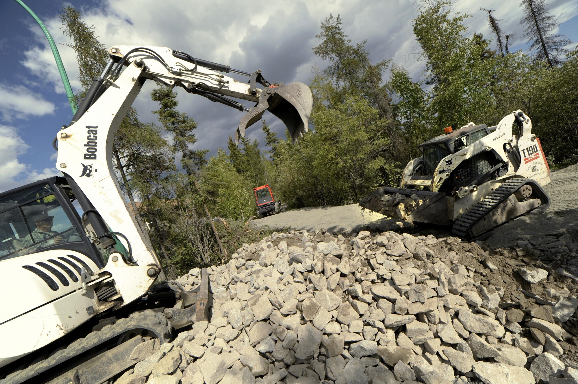 Oregon Air National Guard Chief Master Sgt. Ronald Eckert (left), 142nd Fighter Wing Civil Engineers (CES), operates a excavator to load rock and other materials used to build a new trail at Niven Lake, Yellowknife, Northern Territories, Canada, July 18, 2017. Over 30 CES members are spending two-weeks in Canada working on a variety of projects during their Deployment for Training (DFT). (U.S. Air National Guard photo/Master Sgt. John Hughel, 142nd Fighter Wing Public Affairs)