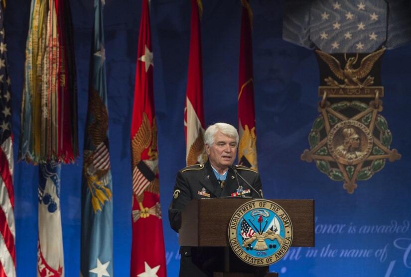 Spc. 5 James C. McCloughan speaks at a podium.