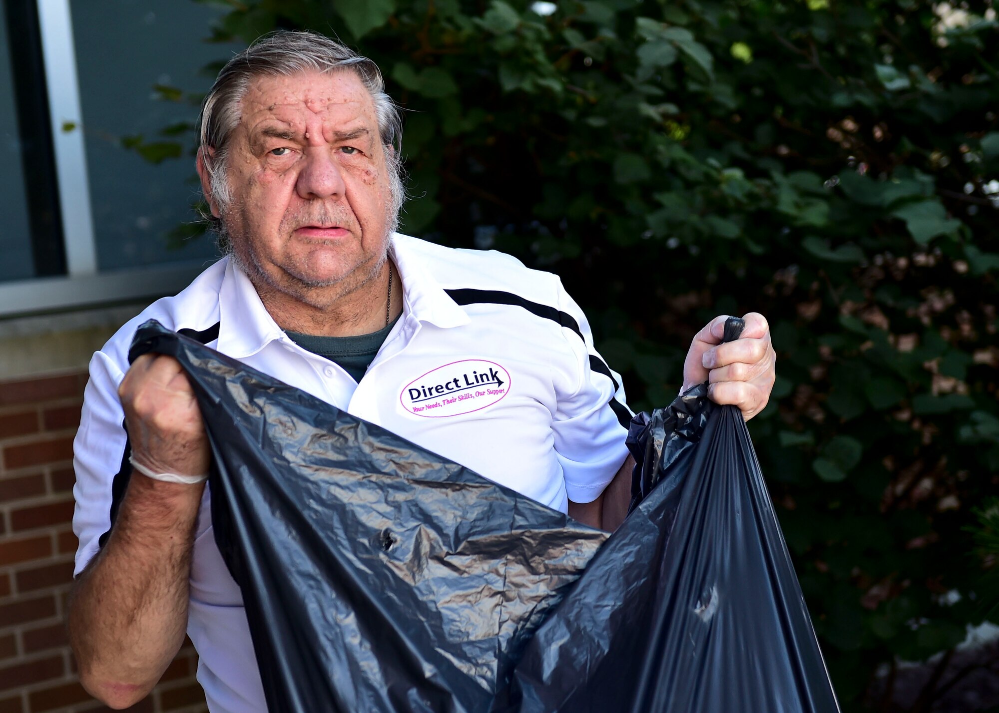 John Morgan, a member of the Direct Link program, ties a garbage bag filled with leaves while volunteering his time July 26, 2017, here. The Direct Link program allows members to get acclimated to different jobs and allow them to work out in the community. (U.S. Air Force Photo by Senior Airman Jeffrey Grossi.)