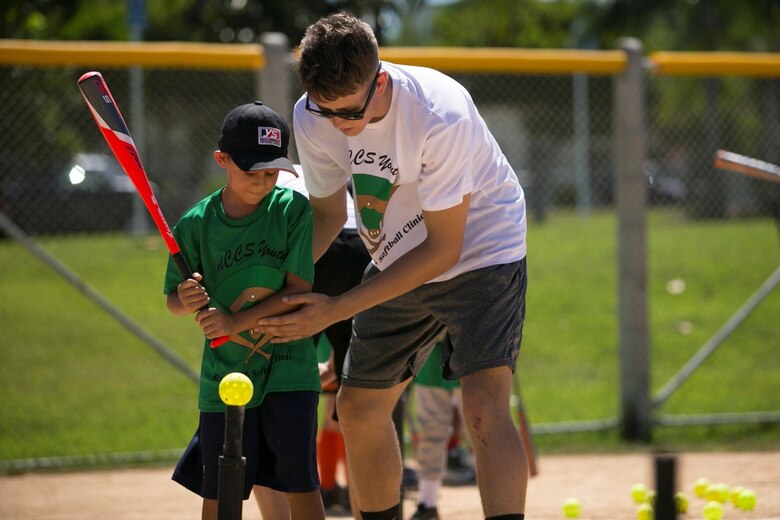 Lance Cpl. Lucas Smith adjusts a child’s batting stance at a youth baseball clinic