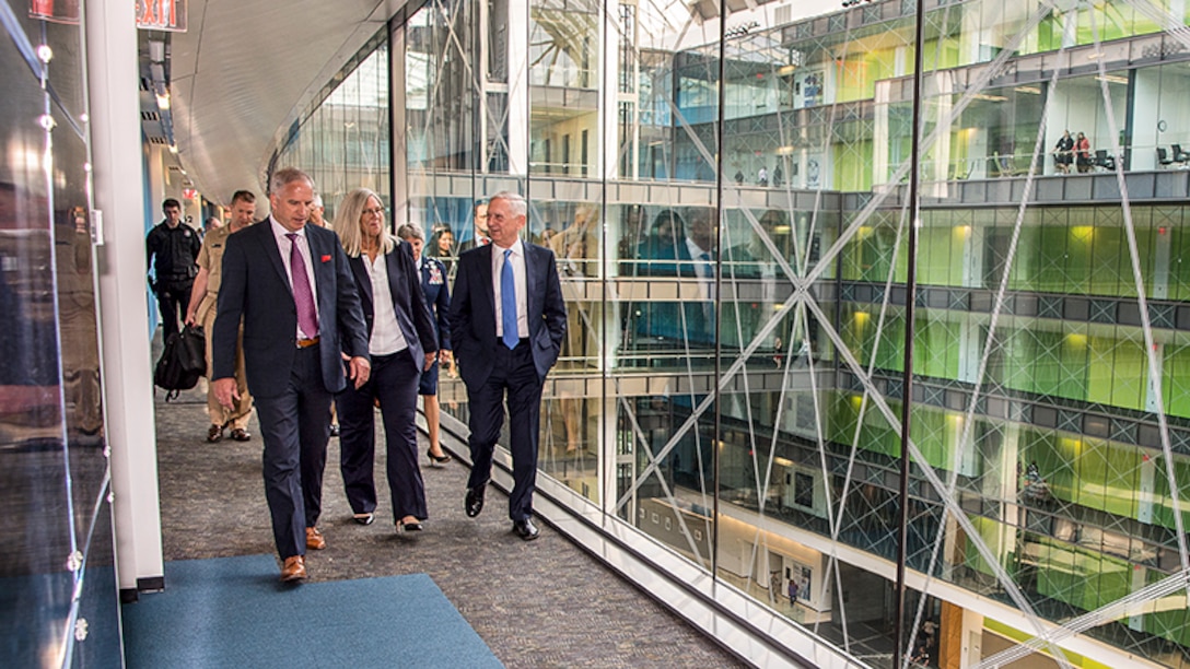 Defense Secretary Jim Mattis walks with agency officials in a building with glass walls.