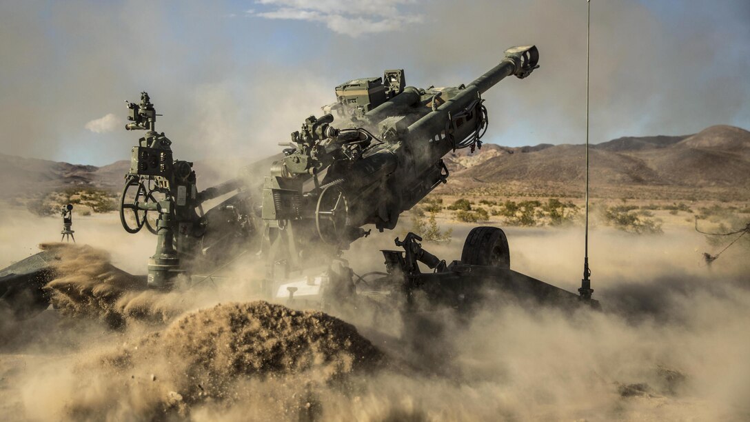 Sand and dust billow around a howitzer.