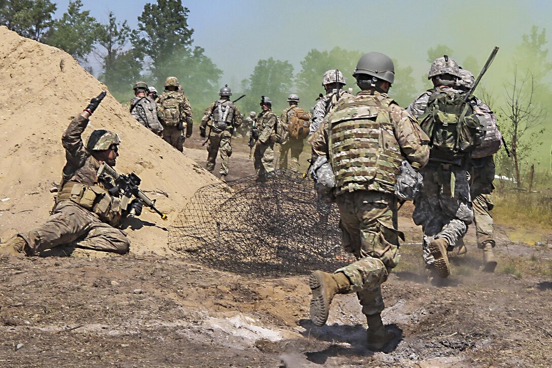 Soldiers run on a dirt path amid a faint greenish-yellow smoke cloud.