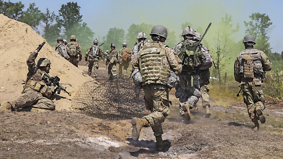 Soldiers run on a dirt path amid a faint greenish-yellow smoke cloud.