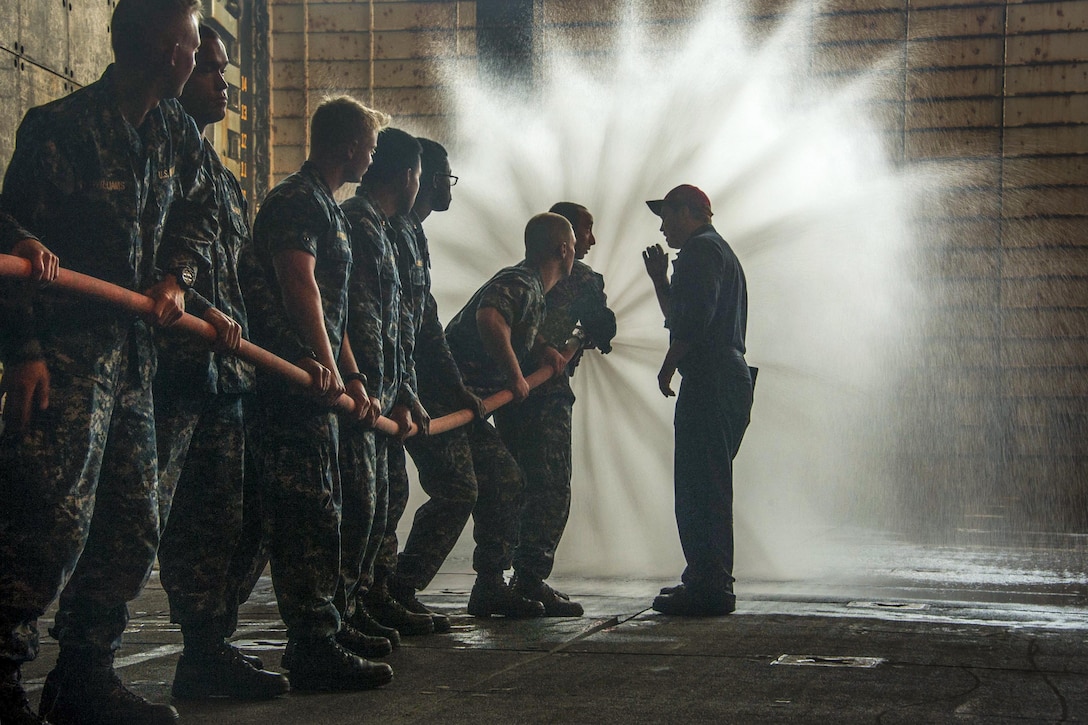 Midshipmen spray water from a hose.