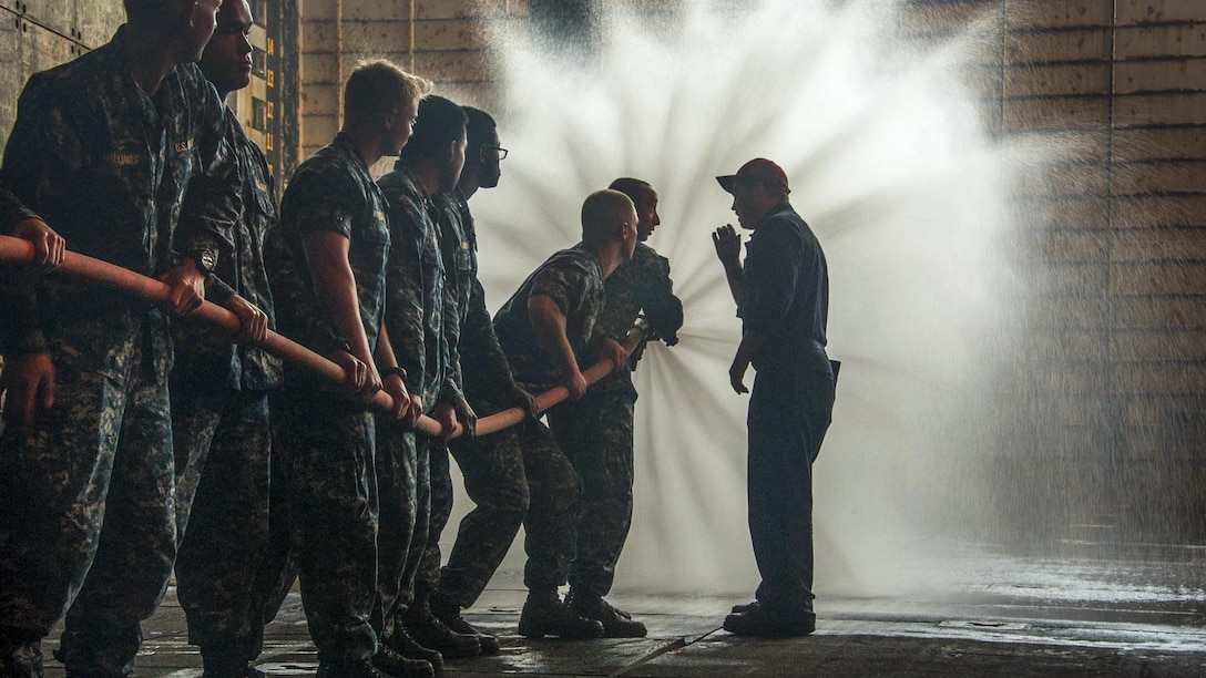 Midshipmen spray water from a hose.