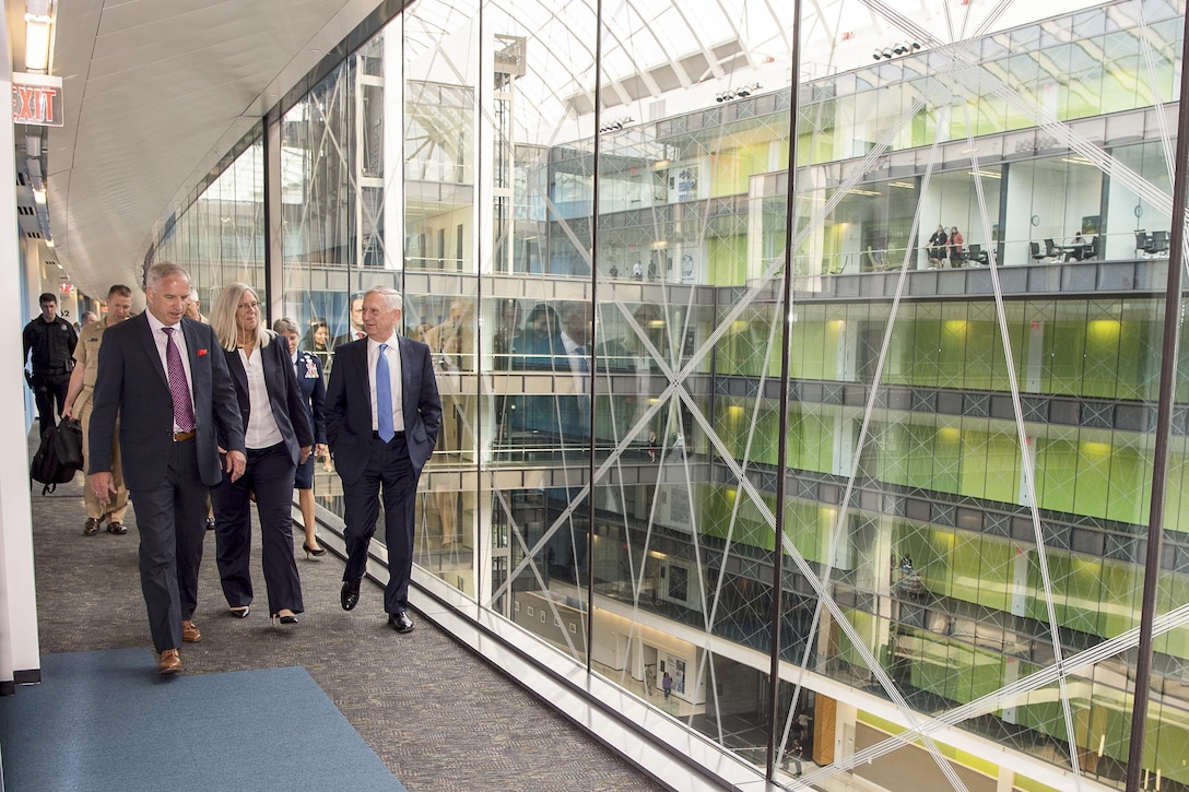 Defense Secretary Jim Mattis walks with other officials in a building with glass walls.