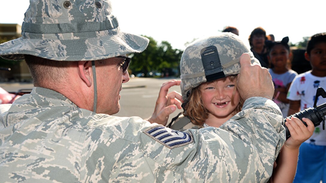 Air Force Tech. Sgt. Keith M. Curtis, a member of the 177th Fighter Wing’s Security Forces Squadron, helps a community member don a security forces helmet during Hamilton Township’s National Night Out at the Hamilton Mall in Mays Landing, New Jersey, on Aug. 1, 2017.