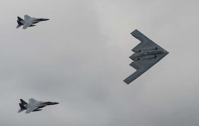 A U.S. Air Force B-2 Spirit Bomber and two F-15 Strike Eagle aircraft fly past spectators