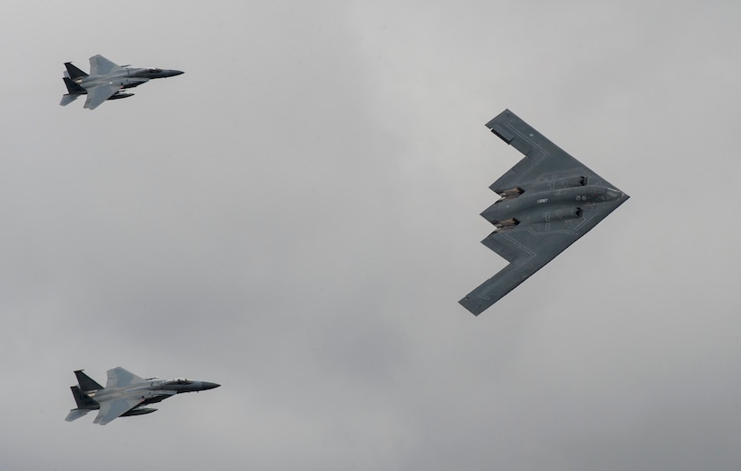 A U.S. Air Force B-2 Spirit Bomber and two F-15 Strike Eagle aircraft fly past spectators
