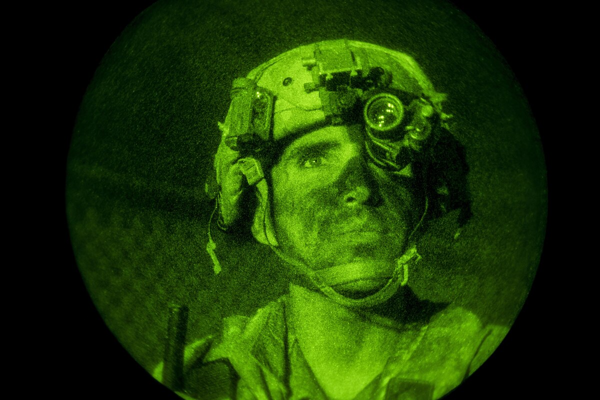 A soldier in a green light watching troops at night.