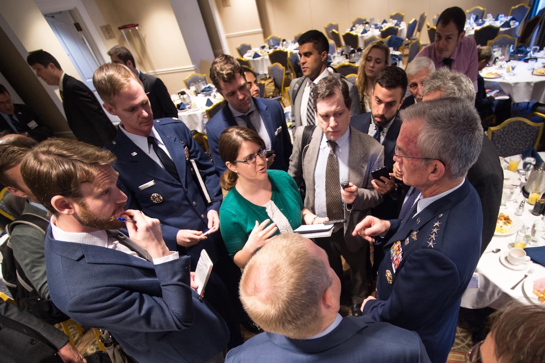 A military leader speaks to a group reporters in a room.
