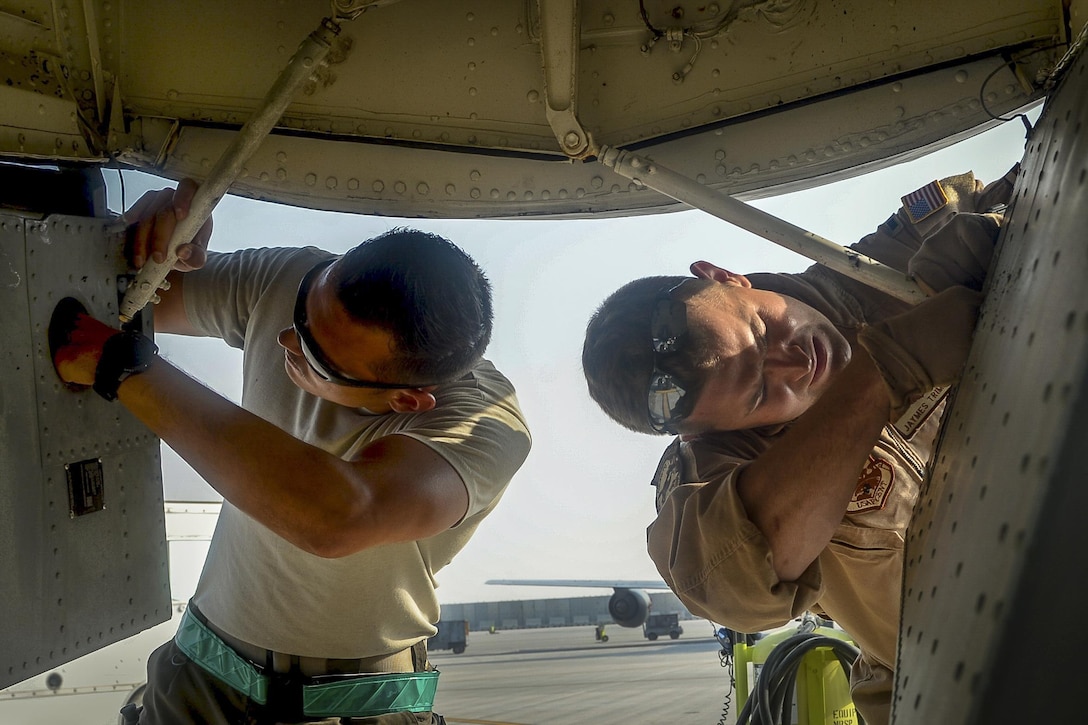 Two airmen inspect the undercarriage of an aircraft