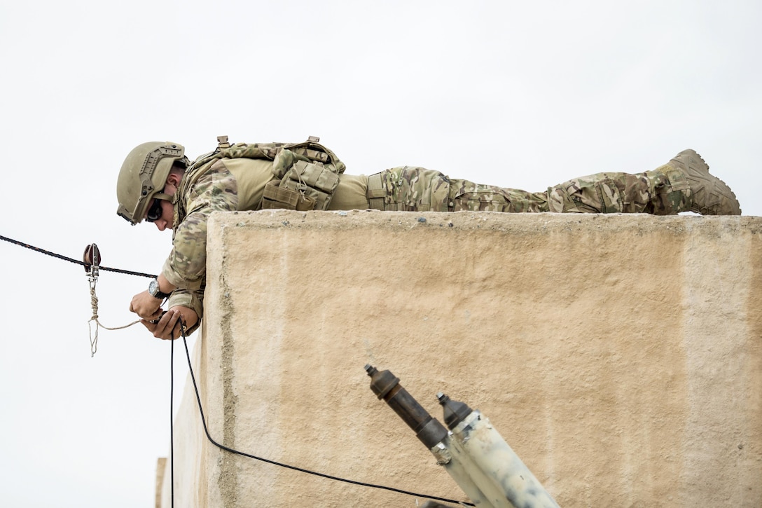 An airman lies on a cement structure while adjusting a rope.