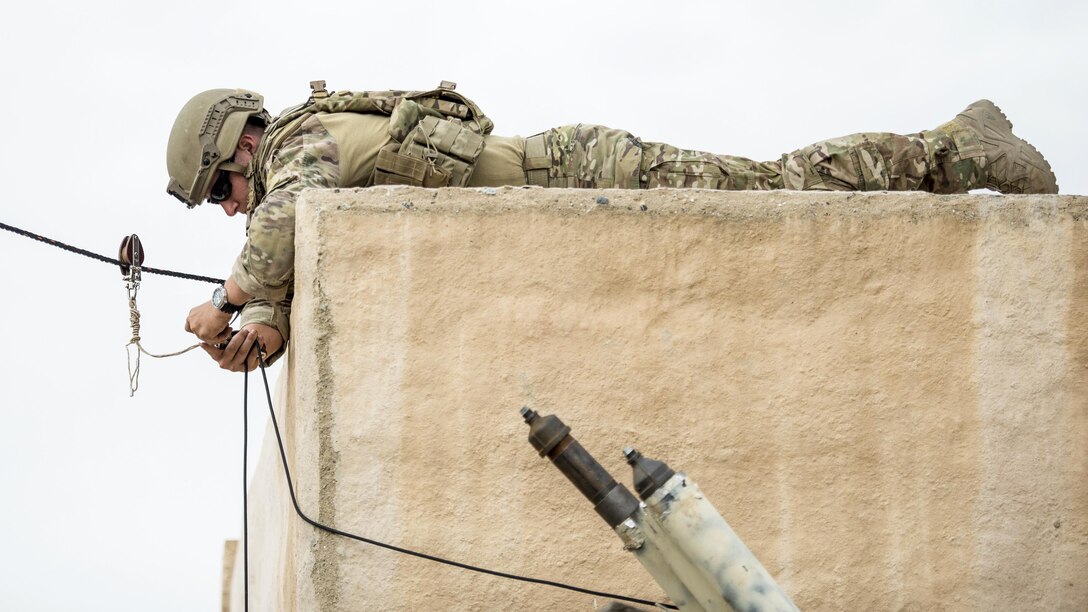 An airman lies on a cement structure while adjusting a rope.