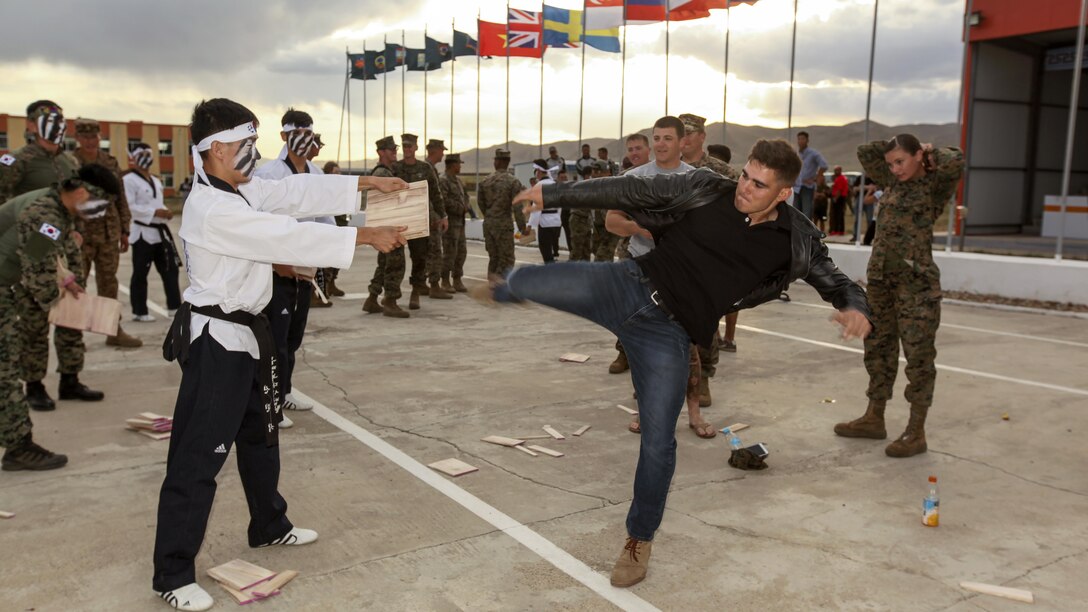 A U.S. service member kicks a wood plank held by a South Korean service member.