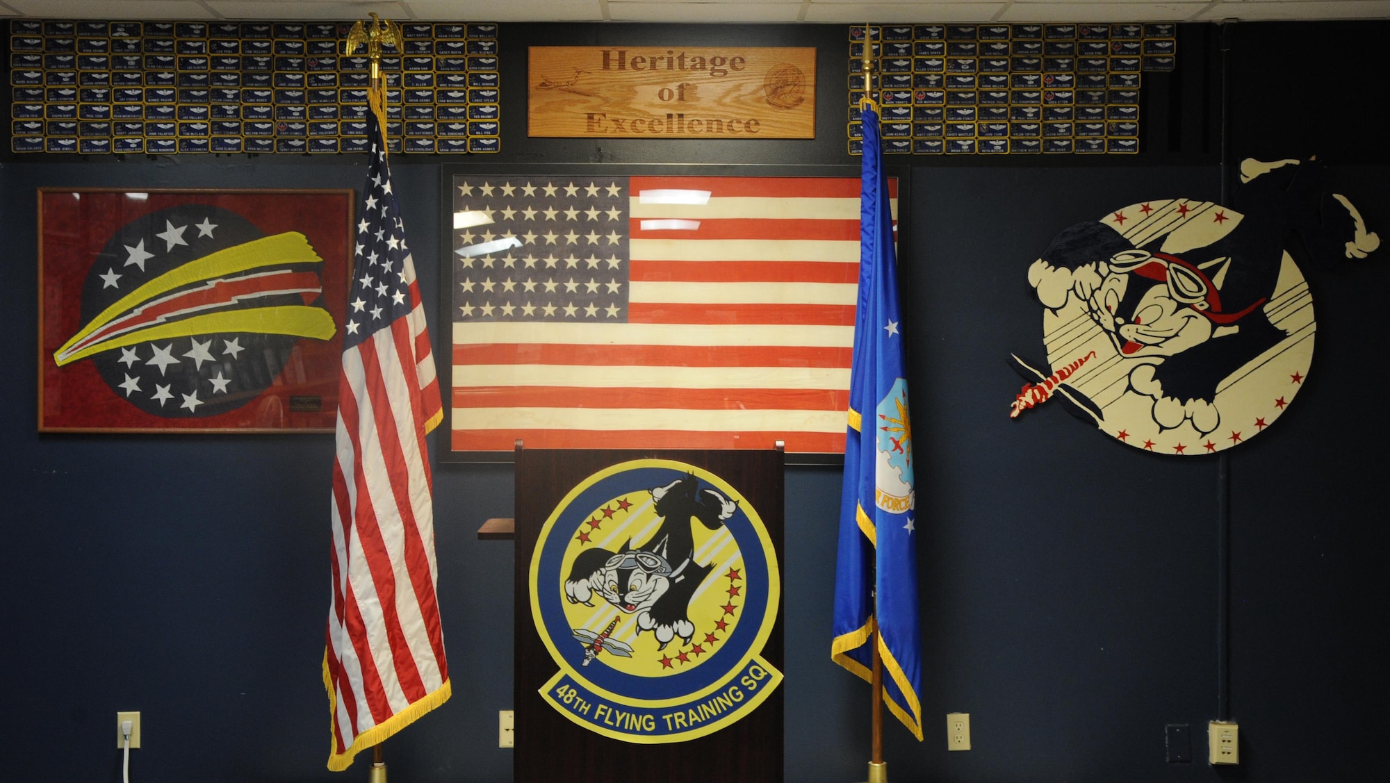 The front of the 48th Flying Training Squadron’s Heritage Room shows the 48th Fighter Interceptor Squadron patch on the left of the American flag and the World War II 48th Pursuit Squadron patch designed by Disney Studios on the right and the current 48th Flying Training Squadron emblem below it. Walt Disney’s team of artists created the patch along with many others for various units as a way to contribute to service members during World War II. (U.S Air Force photo by Airman 1st Class Beaux Hebert)