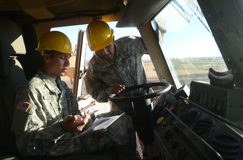 Soldiers in a military vehicle wearing hard hats