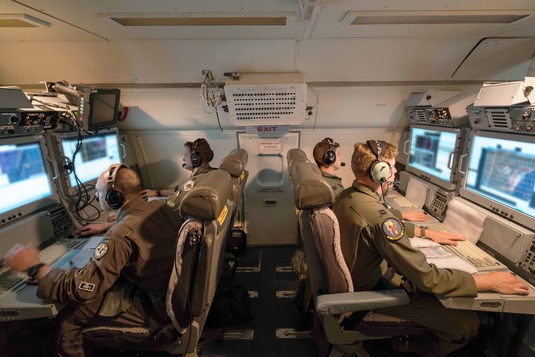 Airmen sit at surveillance monitors on an aircraft.