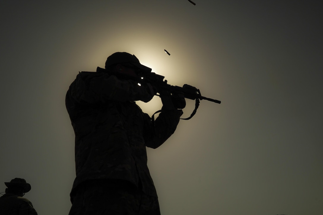 An airman shown in silhouette fires a weapon.