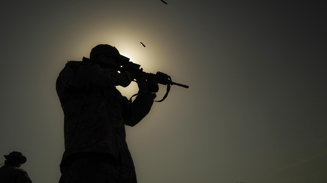 An airman shown in silhouette fires a weapon.