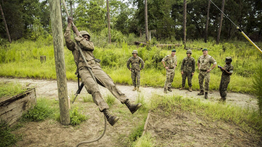 Service members watch a recruit swinging on a rope.