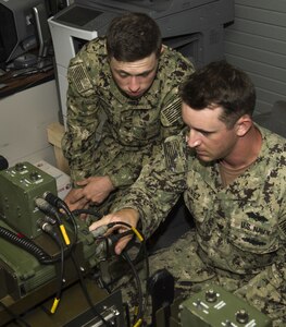 Electronics Technician 3rd Class Codie Flanagan and Electronics Technician 2nd Class Anthony Juarez, assigned to Naval Mobile Construction Battalion (NMCB) 1, adjust frequency codes on a GRC-234 high-frequency base station at Naval Base Guam July 27, 2017. These tests give NMCB 1 Sailors the opportunity to perform quality assurance checks on their system’s maximum range and communication quality with Port Hueneme, Calif. NMCB 1 provides expeditionary construction and engineering support to expeditionary bases and responds to humanitarian assistance disaster relief requests.