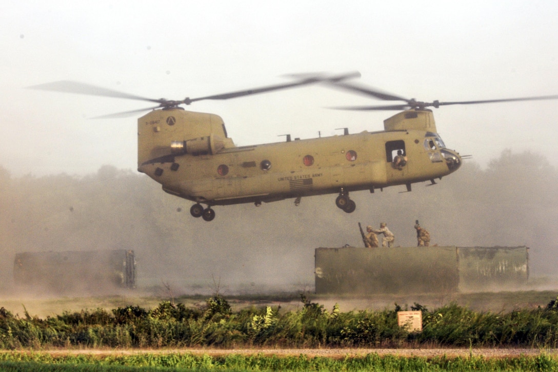 Soldiers on an elevated structure prepare to hook at item to helicopter hovering over them.