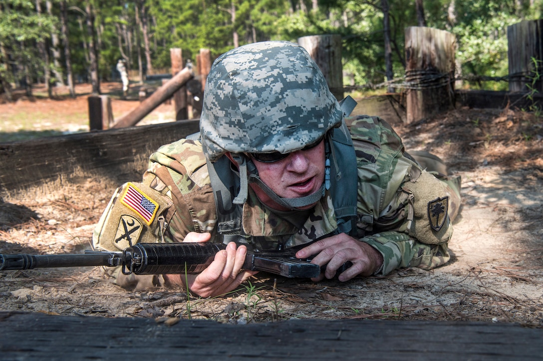 A soldiers maneuvers through wooden obstacles and crawls under barbed wire while participating in pre-deployment training.
