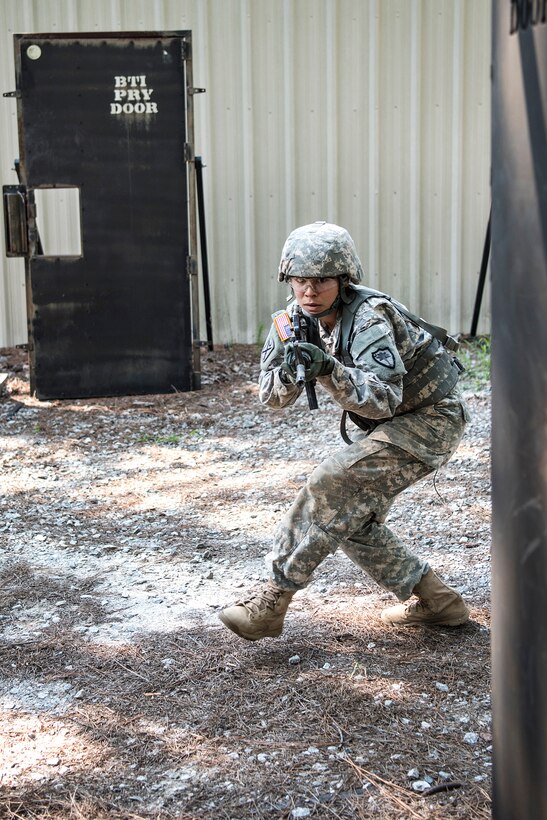 A soldier tactically maneuvers around a wooden structure before entering and searching a building during pre-deployment training.
