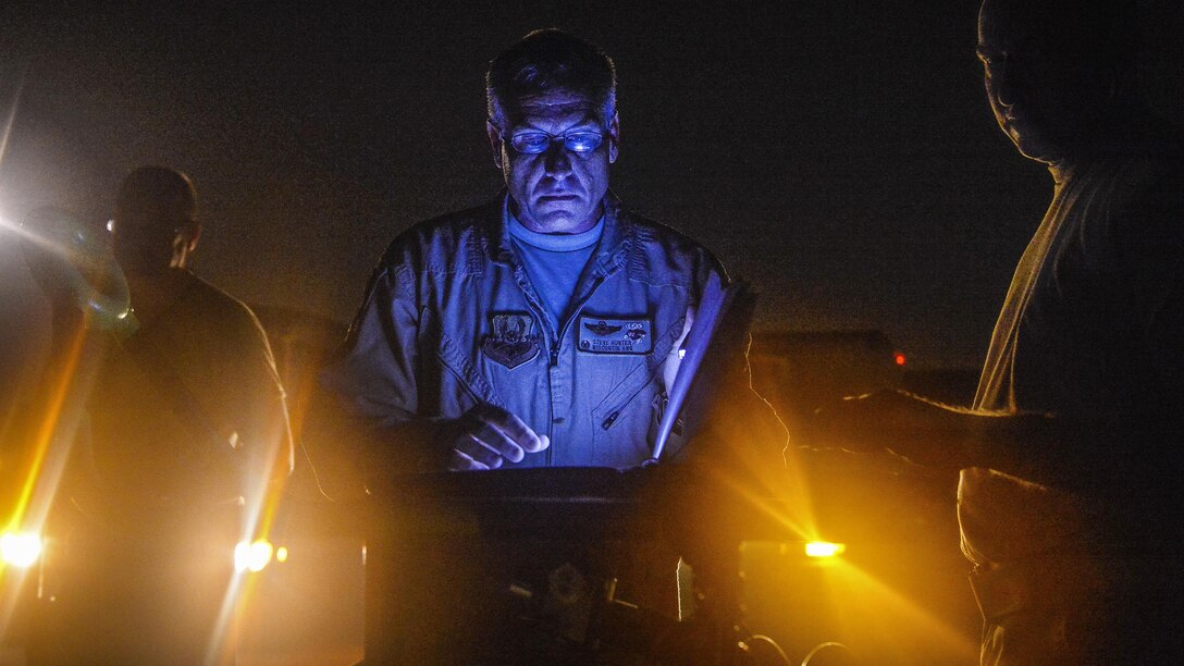 This image shows an airman reviewing records at night as lights shine from below.