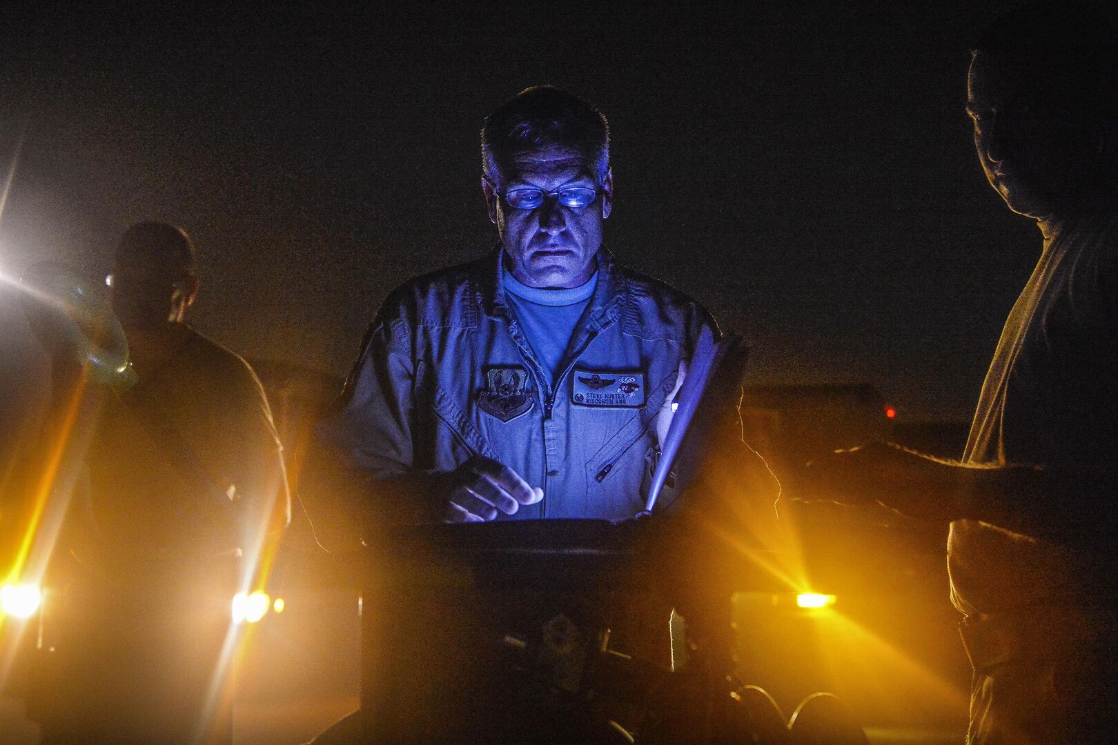 An airman reviews records at night as lights shine from below.