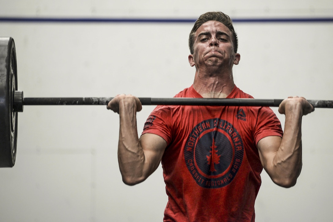 An airman strains while holding a barbell at shoulder height.
