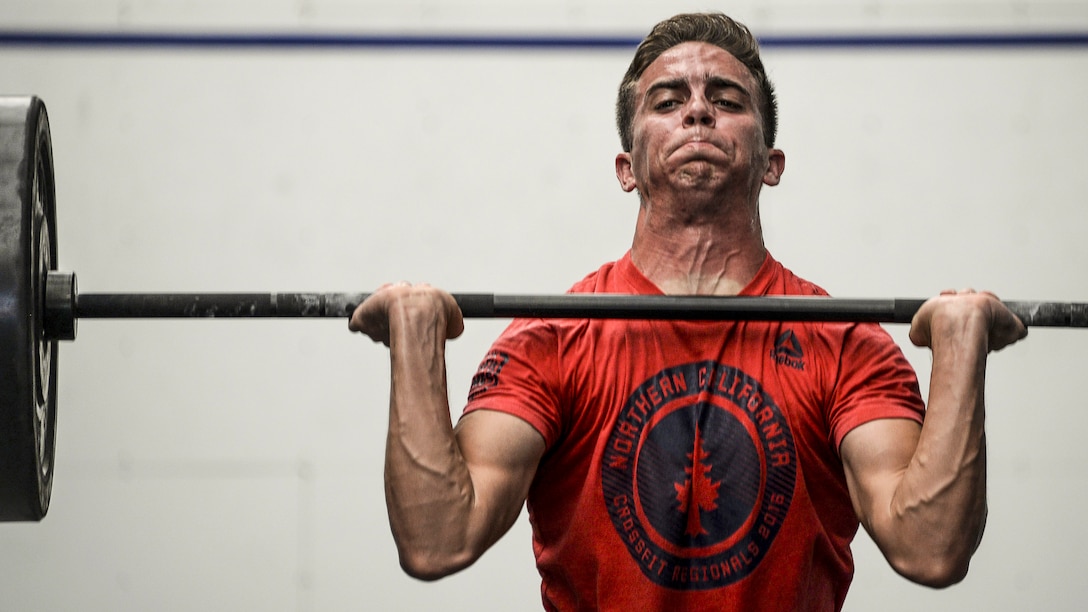 An airman strains while holding a barbell at shoulder height.